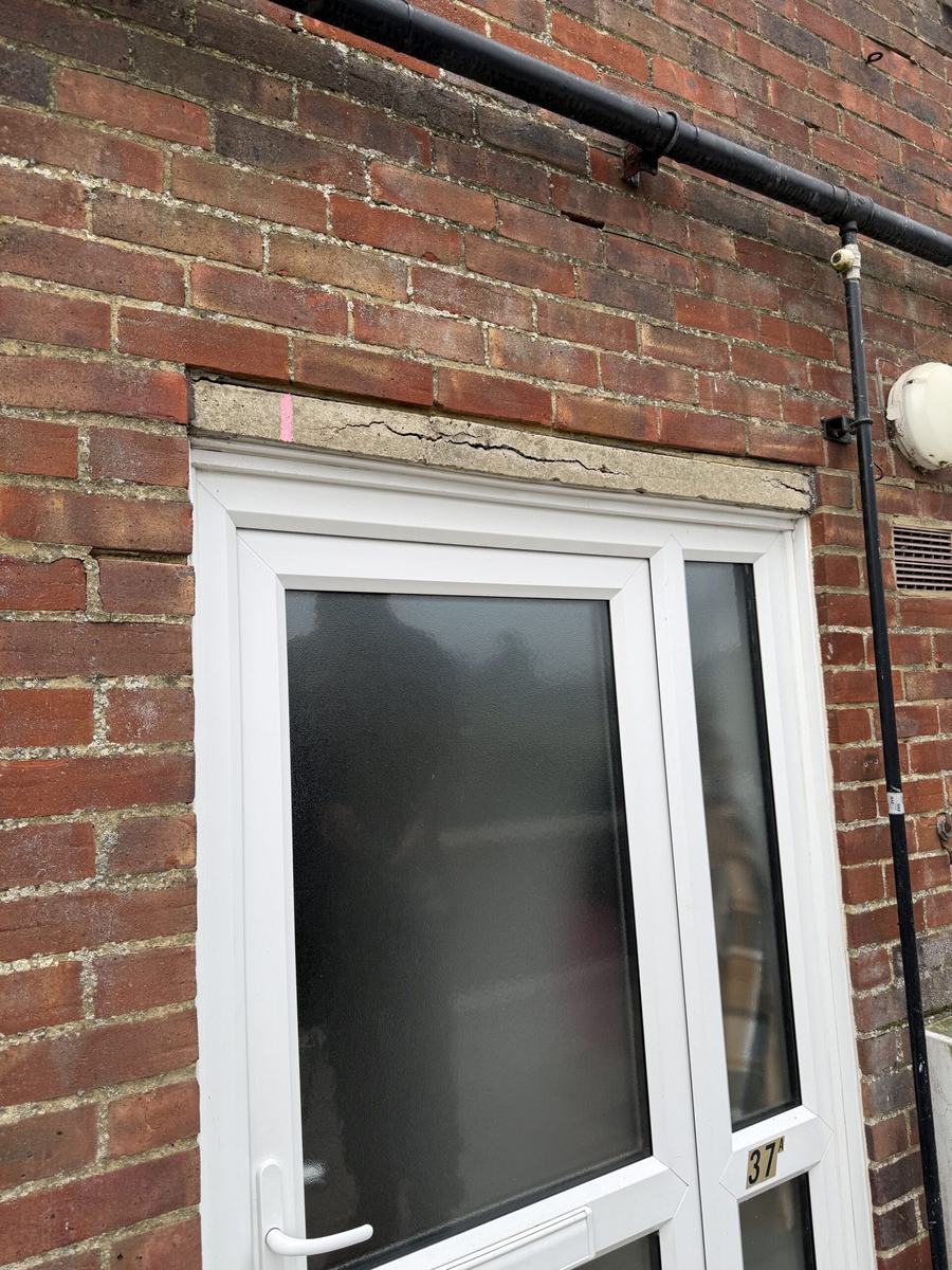 Cracked and spalled concrete boot lintel above a doorway before repair, Polegate